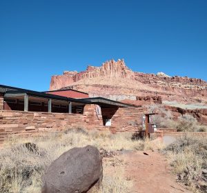 Capitol Reef National Park Visitor Center sits at the edge of red rock formations under a clear blue sky.