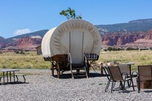 Covered wagon lodging at Capitol Reef National Park, with a white wagon and desert cliffs in the background.