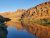 Calm river mirrors orange rock cliffs and blue sky along a narrow canyon in Arches National Park.