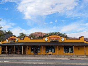 Bright yellow gift shop building with red trim and desert icons in front of Arches National Park, sky and distant red rock.
