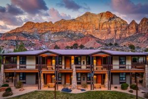 Exterior view of Zion Lodge with lodge balconies, set against dramatic red rock cliffs in Zion National Park.