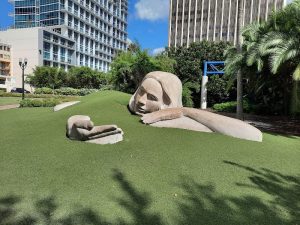 Sculpted reclining figure on a grassy mound with skyscrapers and palm trees in the background near a Biscayne National Park lodging area.