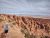 Hiker with backpack and cap walks along a dusty trail beside towering red rock formations in Arches National Park.