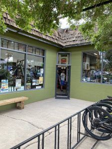 Green shop building with a shingled roof in Arches National Park, bicycles in the windows and a person inside doorway.