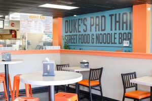 Duke's Pad Thai restaurant interior in Congaree National Park, with bright orange chairs, white round tables, and a bold blue wall sign.
