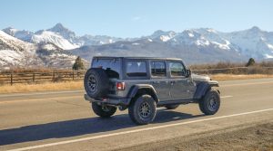 A rugged jeep drives along a mountain highway with snow-covered peaks near Black Canyon of the Gunnison National Park.