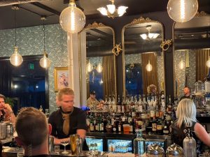 Interior of a speakeasy-style cocktail parlor in Zion National Park, with a long bar, mirrored back wall and warm hanging bulbs.