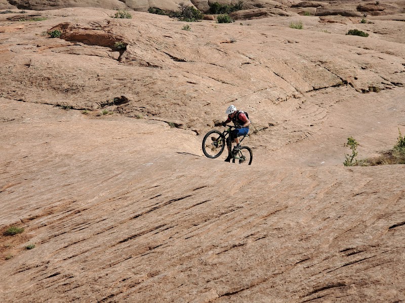 Cyclist wearing a helmet rides a mountain bike across slick sandstone terrain in Arches National Park.