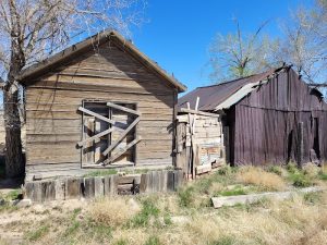 Weathered wooden cabins with boarded windows and rusted siding, dry grasses under a clear blue sky in Arches National Park.