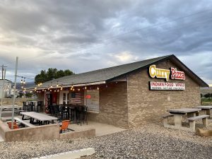 Pizza and Indian food restaurant exterior near Capitol Reef National Park in Torrey, Utah, shown with outdoor seating and string lights.