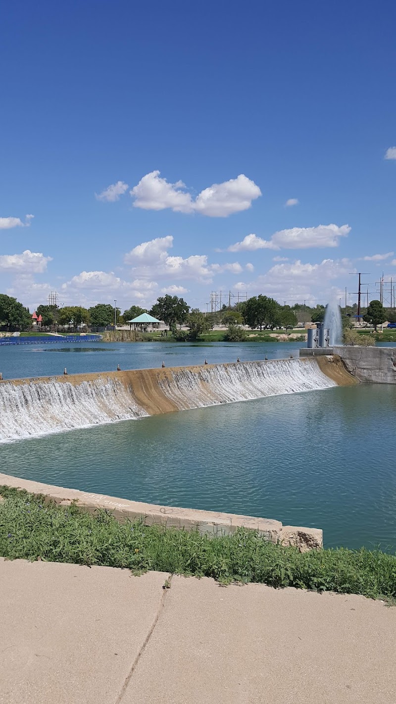 Carlsbad Caverns National Park: view of a park pond with a fountain and dam in a town-area setting.
