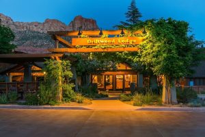 Front entrance of a lodge at Zion National Park, warmly lit at dusk with desert landscaping and canyon rock backdrop.