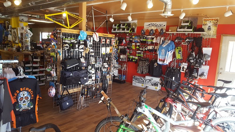 Inside a gift shop at Arches National Park, bicycles on display with helmets, jerseys, bags and cycling gear on racks along orange walls.