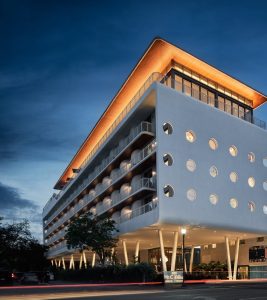 Coconut Grove hotel exterior near Biscayne National Park, a modern white building with circular windows and warm rooftop lighting at dusk.