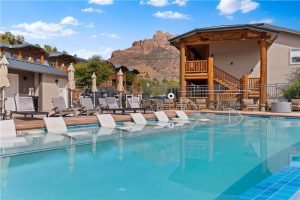Sunny pool area at a Springdale lodging near Zion National Park, with lounge chairs, umbrellas, turquoise water, and views of red rock canyon walls.