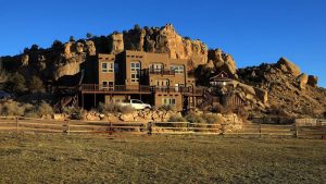 Slot Canyon lodge perched against rugged rock cliffs in Capitol Reef National Park, with a desert foreground and clear blue sky.