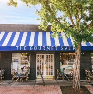 Congaree National Park storefront restaurant along a brick sidewalk under a blue-and-white striped awning, with trees nearby.