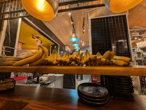 Interior of Zion National Park restaurant with a wooden counter, bananas lined up, and colorful pendant lights overhead.