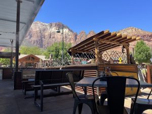 Patio seating at a Zion National Park restaurant with red rock cliffs in the background.