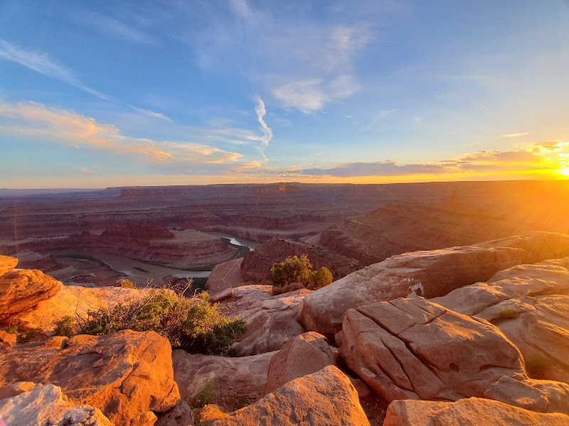 Sunset over layered sandstone cliffs and a winding river at Dead Horse Point in Arches National Park, with warm orange rock and blue sky.