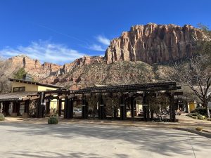 Lodge complex exterior at Zion National Park with a wooden pergola and towering sandstone cliffs behind.