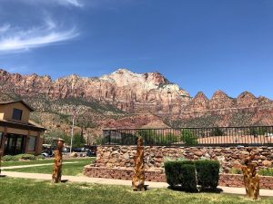 Bumbleberry Inn area in Zion National Park with red sandstone cliffs rising behind a stone patio and green lawn.