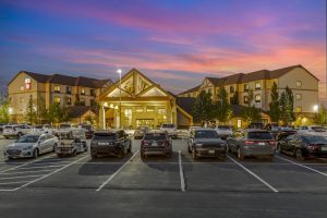 Front exterior of Bryce Canyon Grand Hotel at twilight, with a bright entryway and a large parking lot in front.