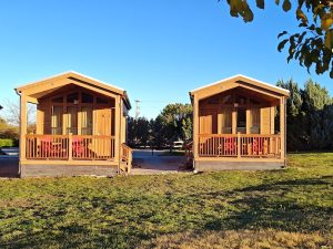 Two wooden lodge cabins with porches and red chairs sit side by side in Capitol Reef National Park’s lodging area.