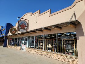 Gift shop storefront with adobe façade, large glass windows, and wooden beams under a clear Arches National Park sky.