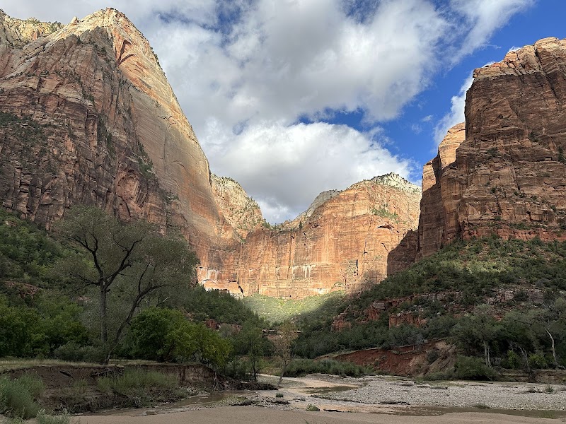 Temple of Sinawava in Zion National Park rises above the Virgin River canyon with red cliffs and a blue sky.