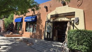 Arches National Park gift shop with blue awning, adobe walls, steps to entrance, and visitors inside.