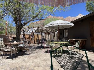 Outdoor dining patio at The Park House in Zion National Park with colorful chairs, umbrellas, and a desert backdrop under blue skies.