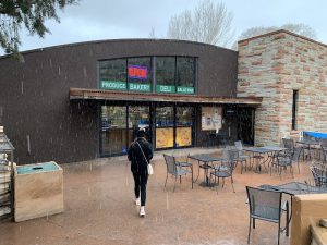 Market storefront at Zion National Park with open sign, snow falling, and outdoor seating outside.