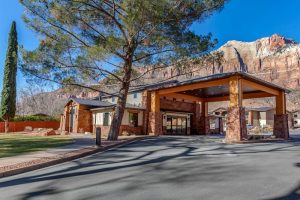Lodge entrance at Zion Canyon Inn & Suites near Zion National Park, with stone columns and red canyon walls in the background.