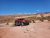 Red Jeep Wrangler on a rocky 4x4 trail in Arches National Park amid desert scrub and distant mesas under a clear blue sky.