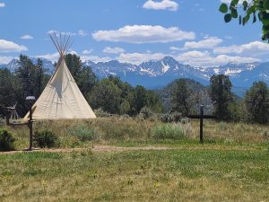 Tipi at a visitor area with a cross in the foreground and snow-capped mountains rising behind in Black Canyon of the Gunnison.