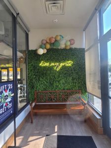 Interior dining area at Congaree National Park featuring a green hedge wall and a yellow neon sign above a wooden bench.