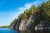 Photograph of granite cliffs topped with trees alongside a blue lake.