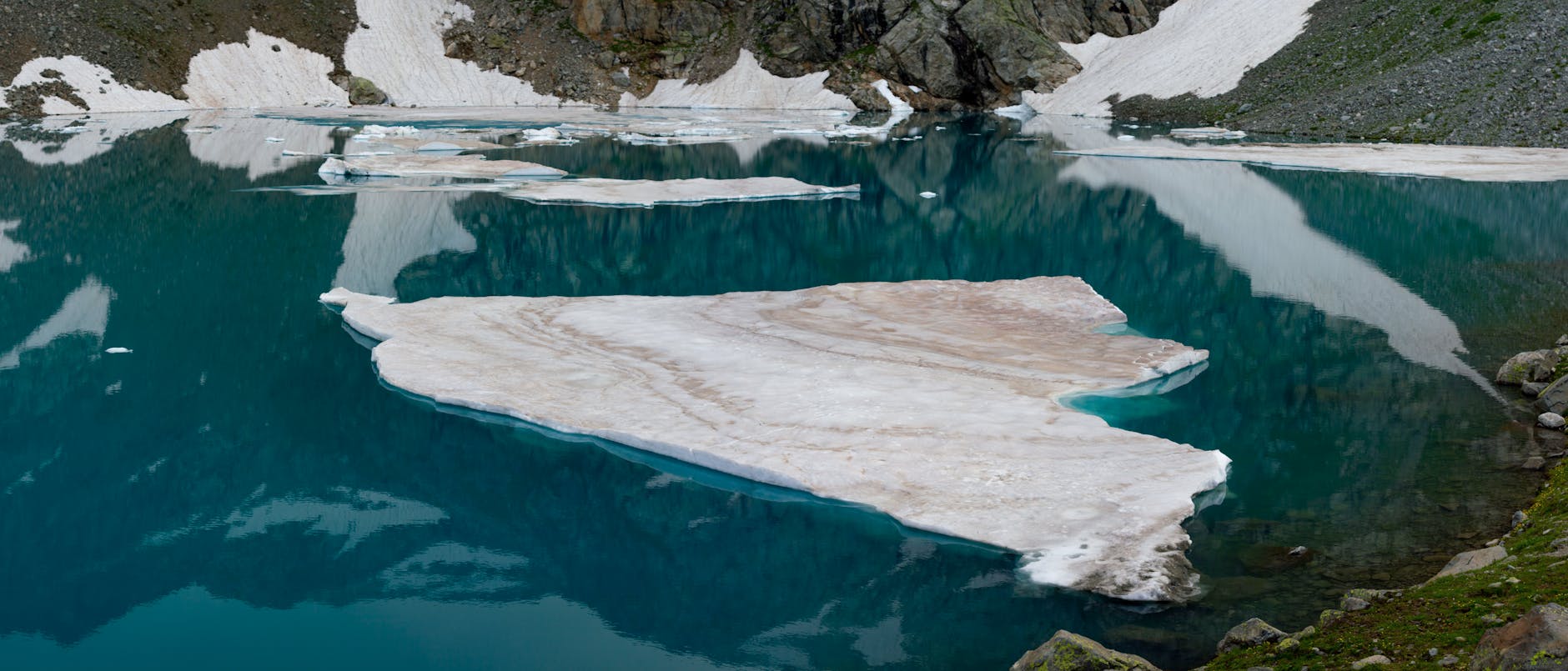 Captivating view of a mountain lake partially frozen over, reflecting its icy surroundings.