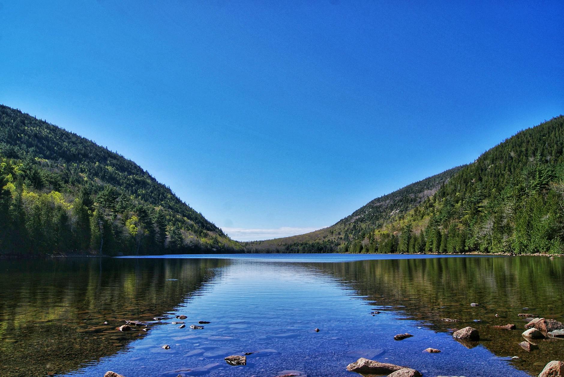 Serene view of Jordan Pond in Acadia National Park with clear reflections and blue sky.