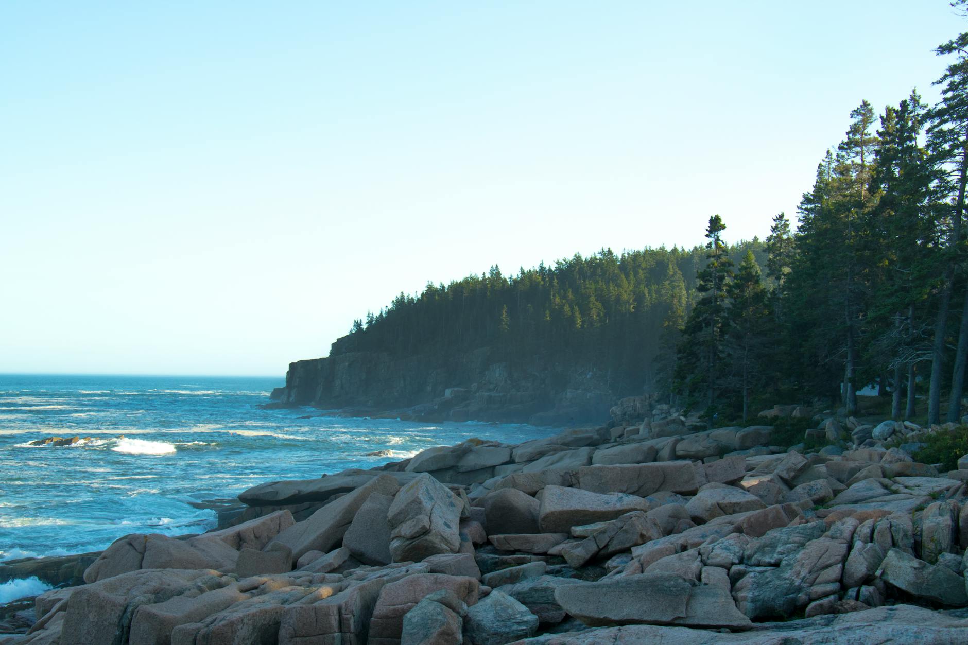 Stunning view of the rocky Acadia coastline with ocean waves crashing against the shore at sunrise.