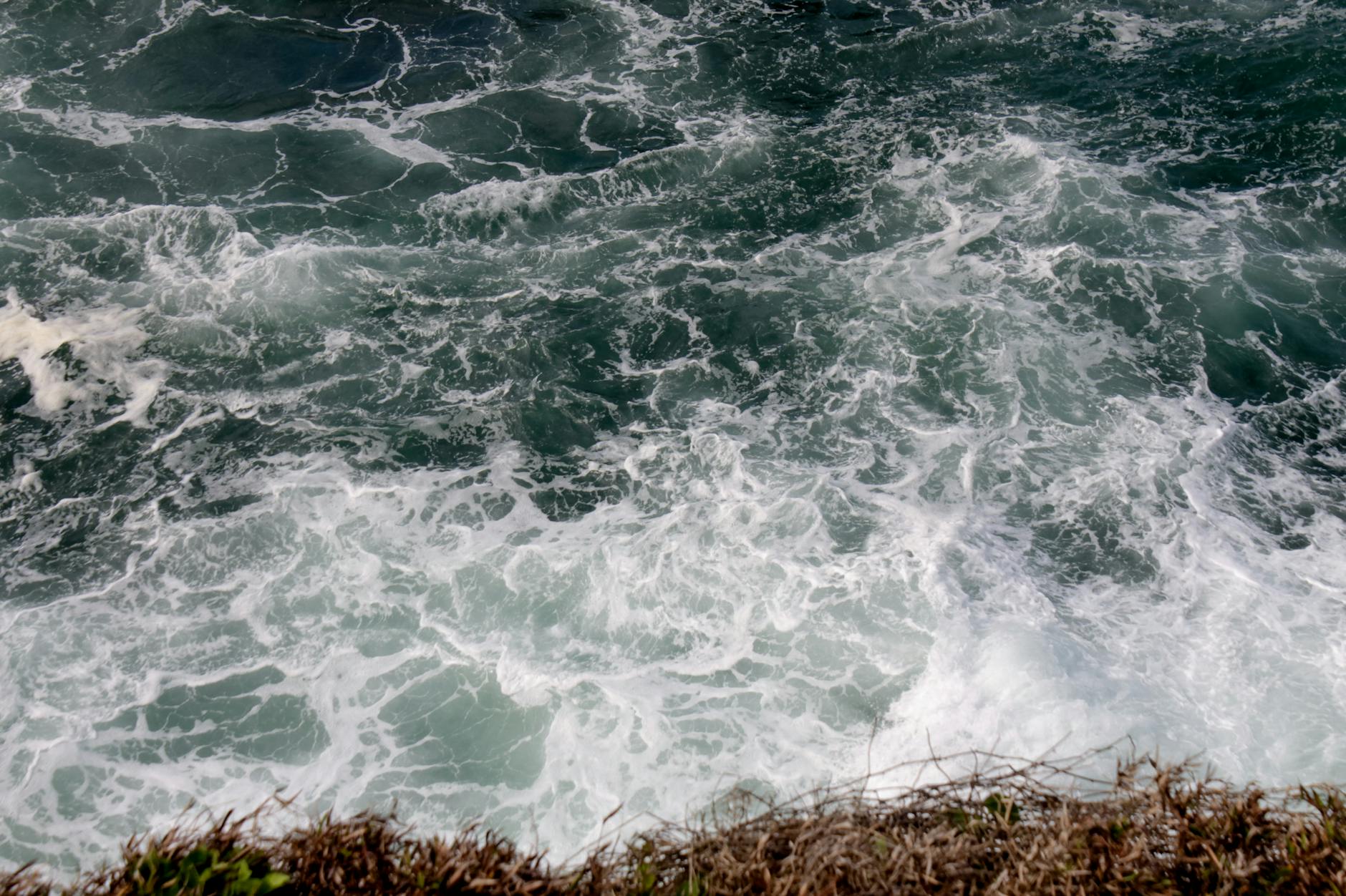 Aerial view of powerful ocean waves crashing onto a rocky shoreline with foamy waters.