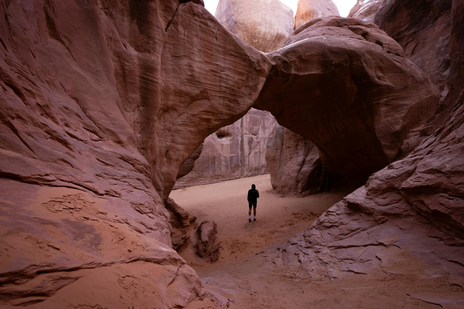 A hiker stands beneath prominent rock formations in Arches National Park, Moab, Utah.