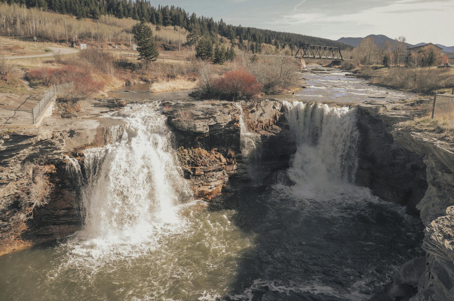 Scenic view of a waterfall cascading over rocks with a bridge in the distance.