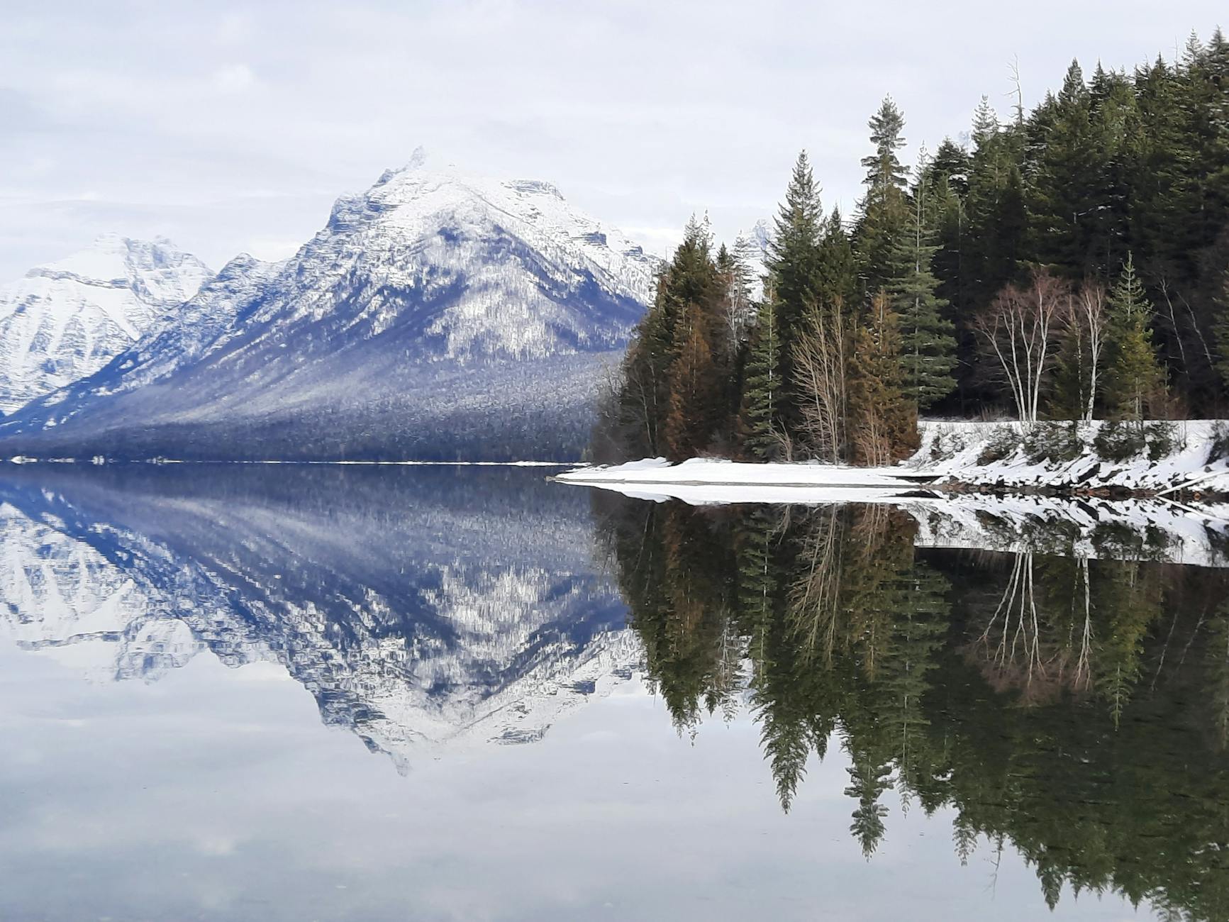 Serene landscape of snow-covered mountains reflecting in a calm lake in Montana, USA.