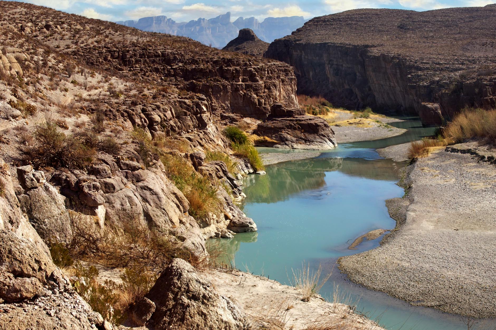 Stunning view of a canyon with turquoise river winding through arid landscape, framed by rugged rocky cliffs.
