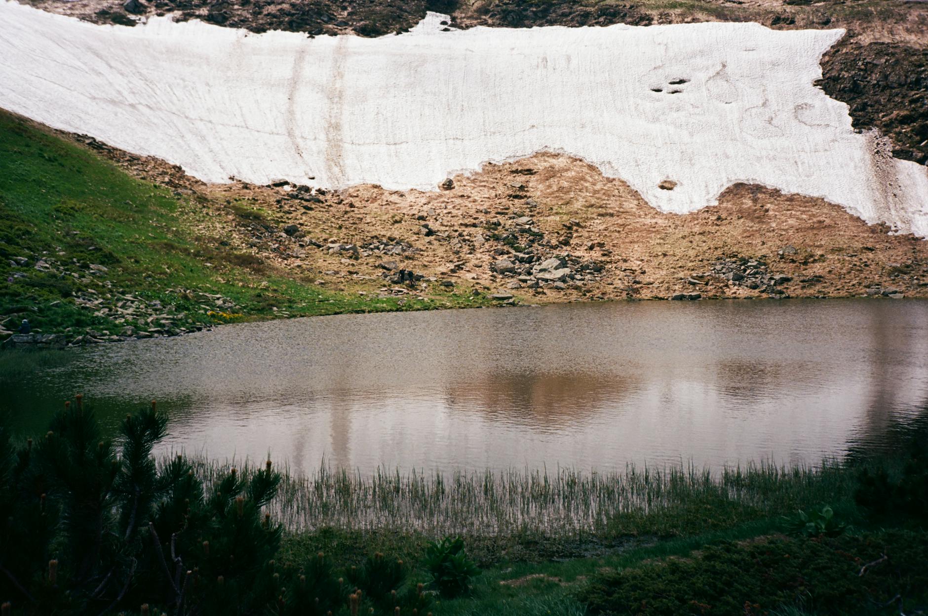 Serene mountain lake with melting snow and lush greenery in a tranquil setting.