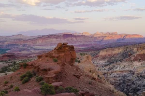 Colorful red rocks, striped cliffs, mountains in the distance, and a pale blue moving to purple sky.