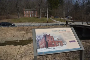 “Frazee Family” panel; behind it, across a water-filled canal and a road, a historic brick house.