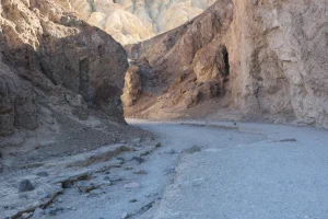 Tan canyon walls tower above a gravel wash which curves to the left deeper into the canyon.